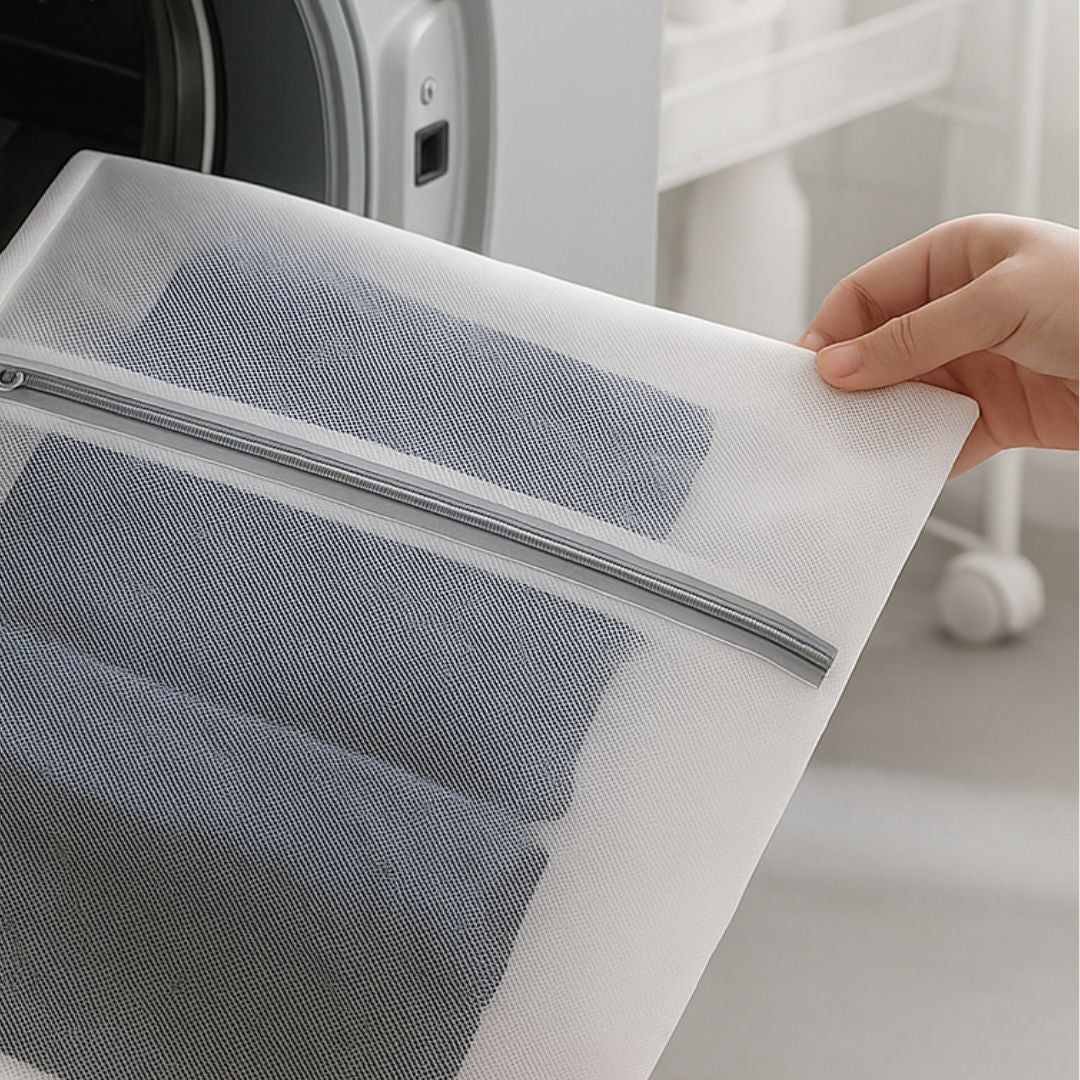 Hand holding a mesh laundry bag in front of a washing machine.